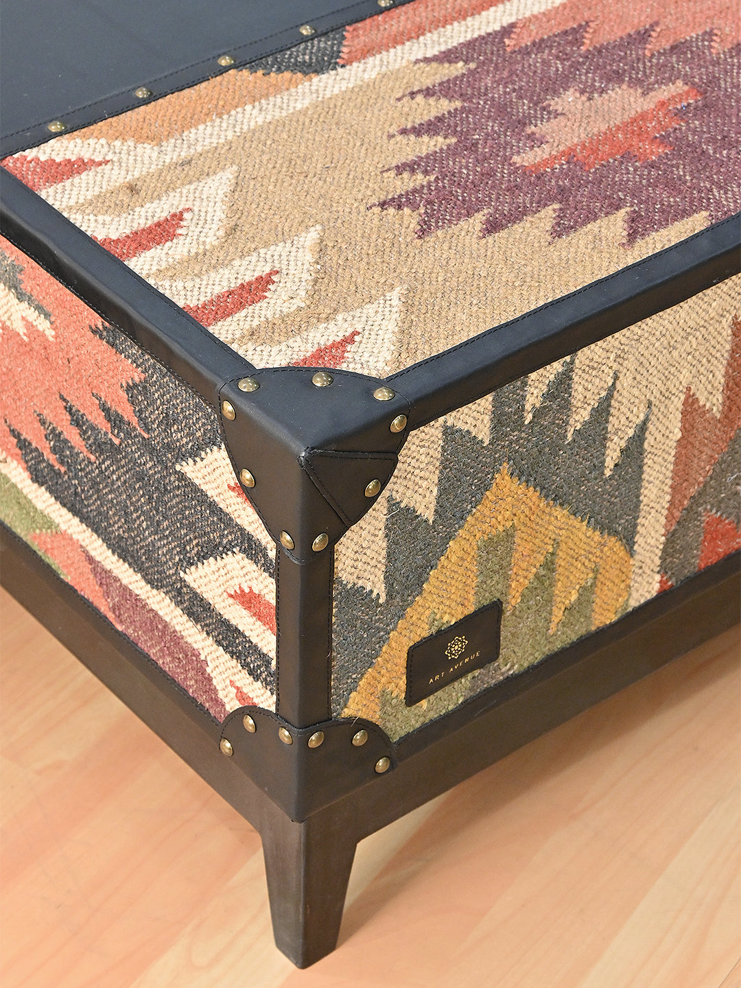 Close-up of a stitched black leather corner cap with brass studs where the kilim top meets the kilim flank