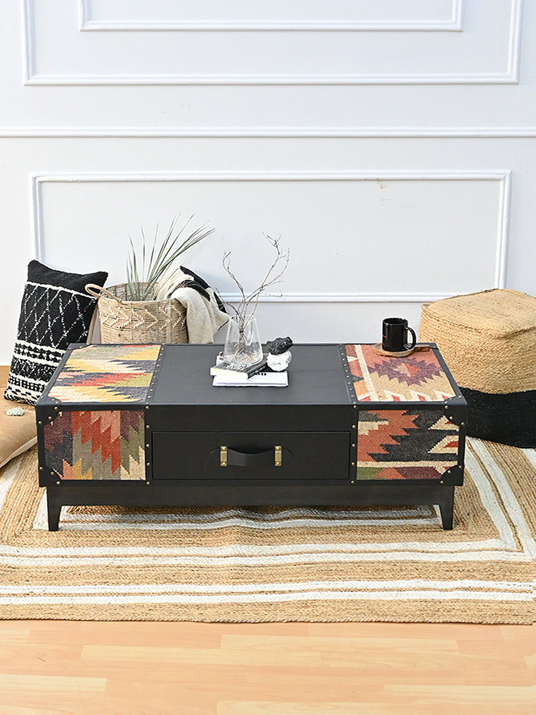 Kumbhalgarh kilim and black leather coffee table styled on a striped jute rug with a glass vase, books and a jute pouf