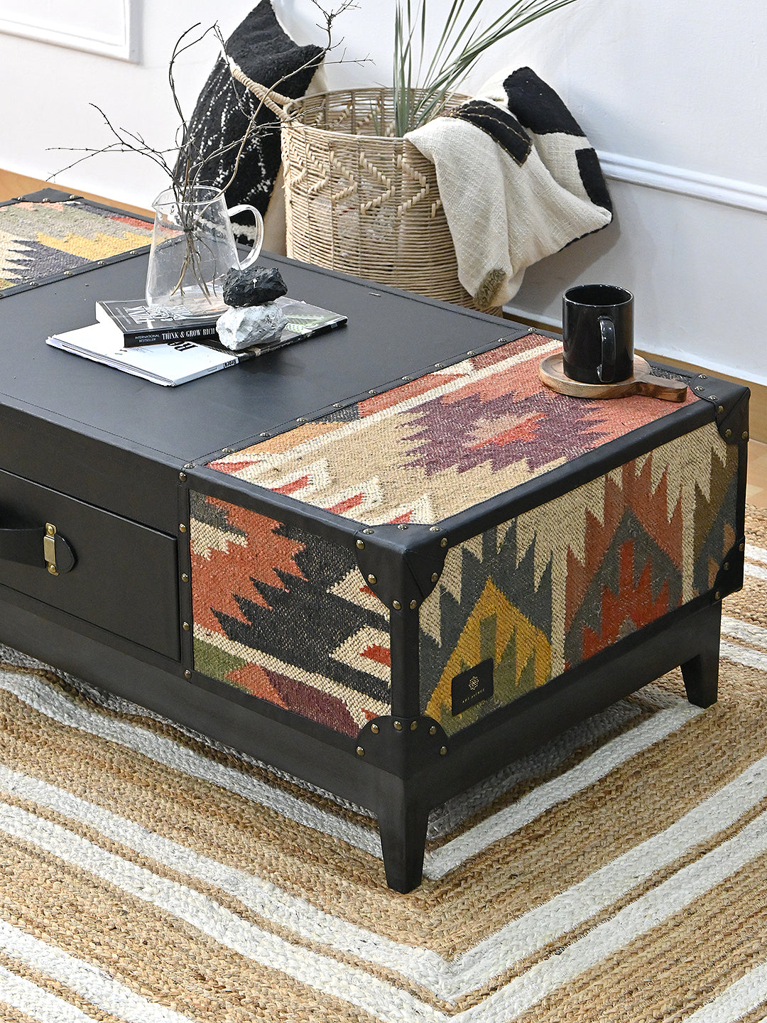 Close view of a Kumbhalgarh kilim top panel with a coffee mug, beside the black leather centre and the Art Avenue maker's tag