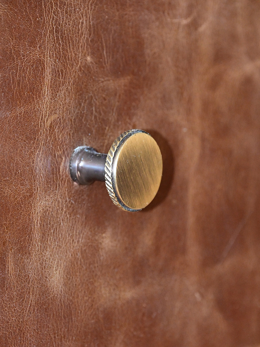 Detail of a knurled brass drawer knob on distressed leather, Alsisar wardrobe