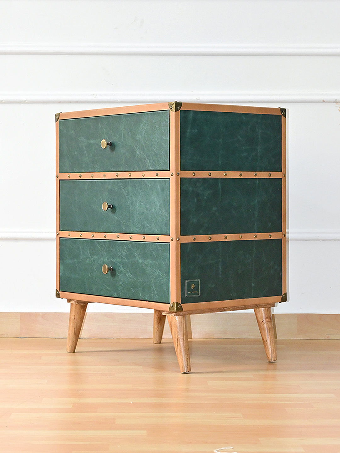 Sariska chest of drawers at a three-quarter angle, the tan studded bands continuing around the green leather side and the Art Avenue maker's tag