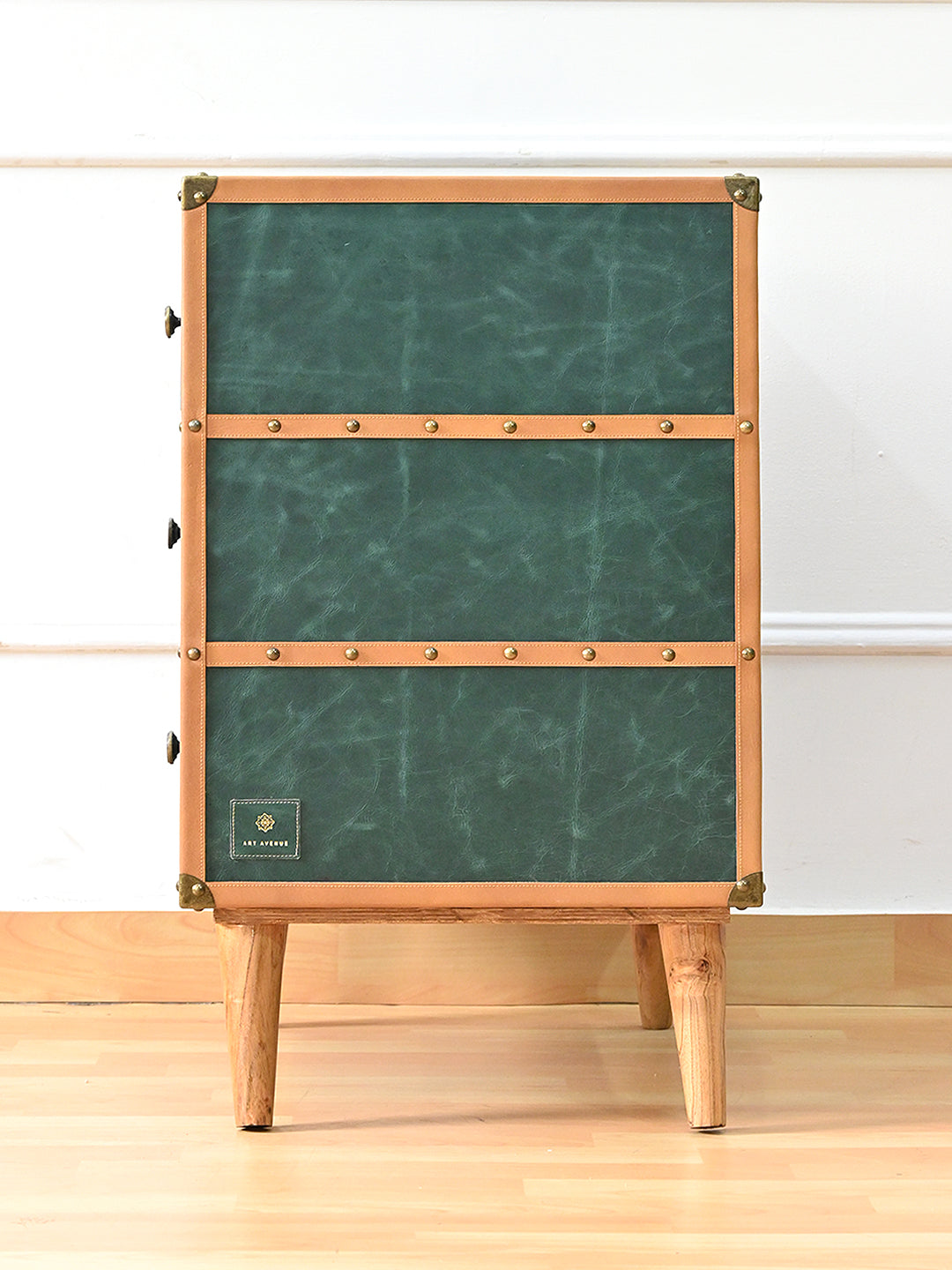 Side view of the Sariska chest of drawers — green leather panels divided by tan studded bands, with the maker's tag