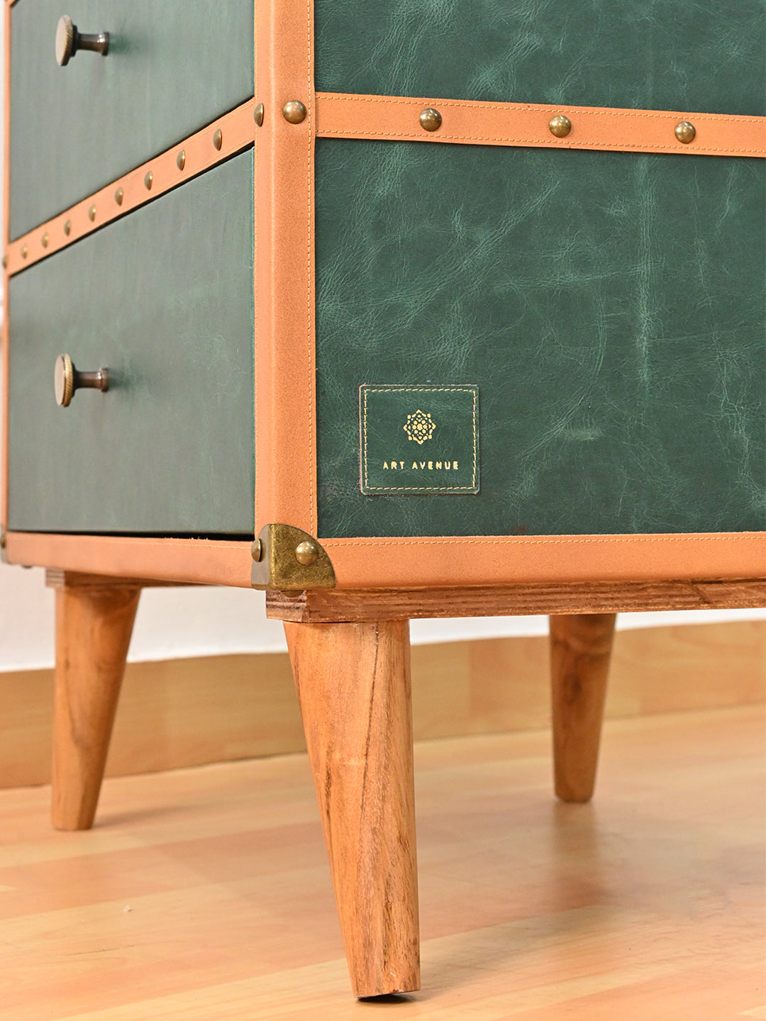 Art Avenue maker's tag stitched onto the green leather side, above a metal corner cap and tapered solid wood leg