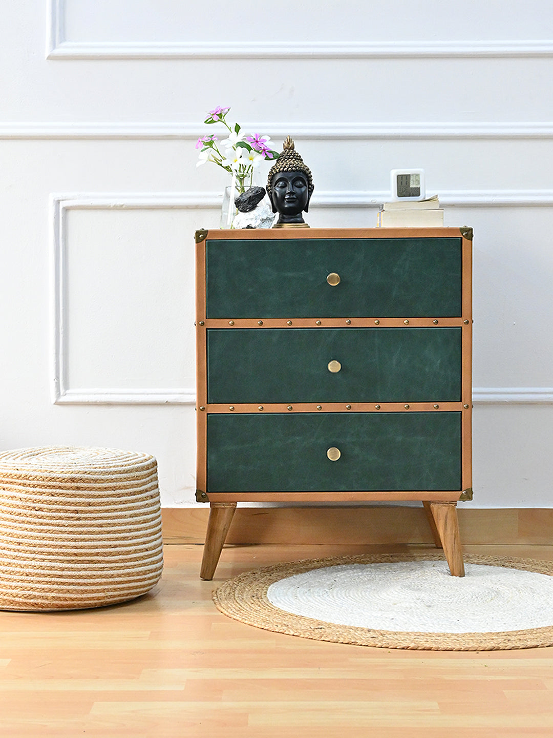 Sariska green leather chest of drawers styled with a Buddha head, orchids and a clock beside a jute pouf and round rug