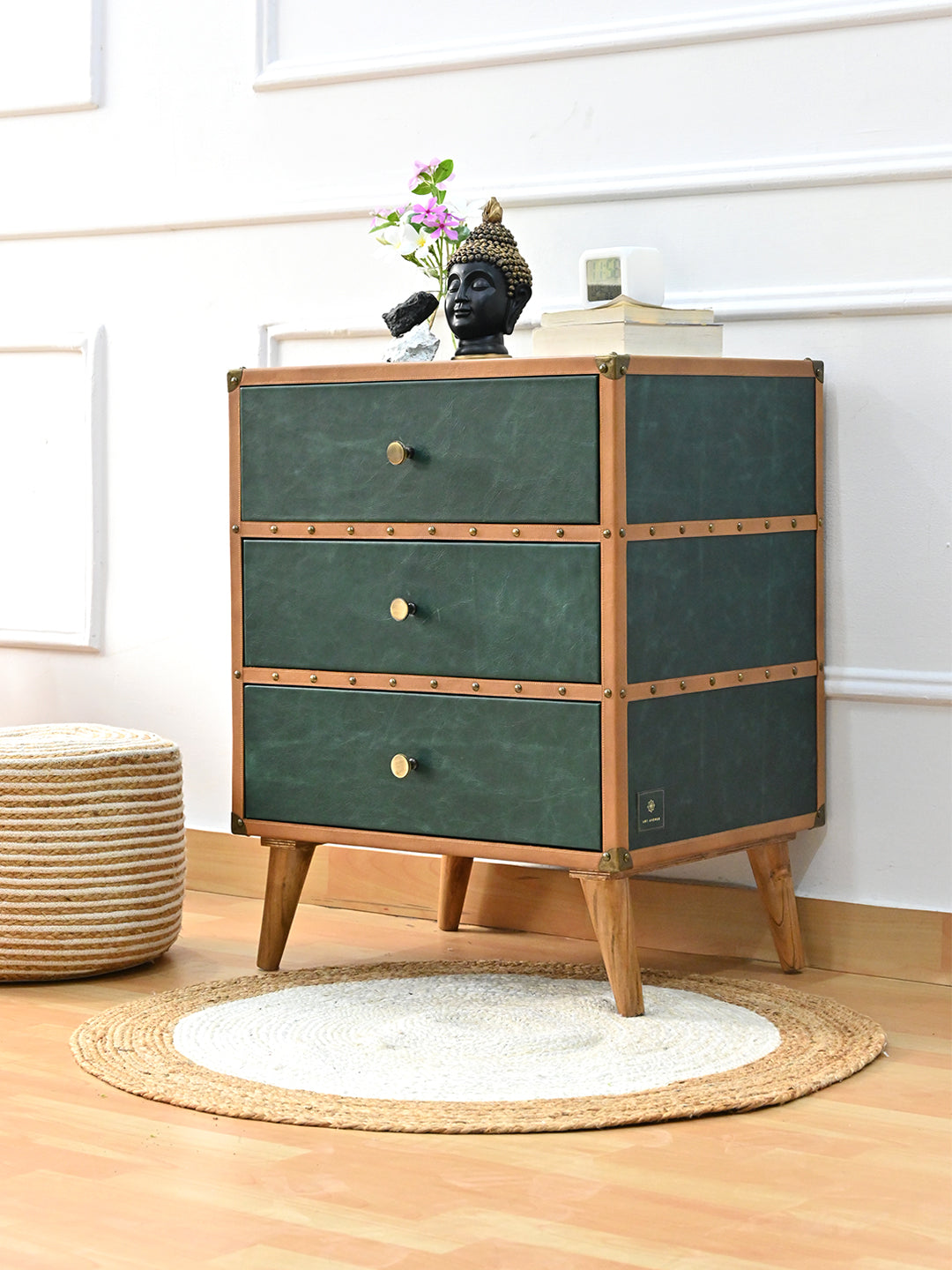 Sariska green leather chest of drawers styled at an angle on a round jute rug, beside a woven pouf