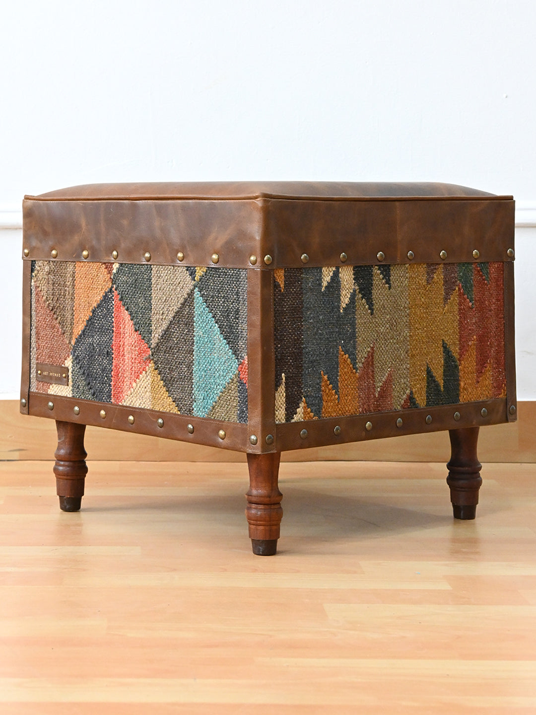Dundlod kilim and leather ottoman by Art Avenue, three-quarter view showing two different kilim faces and studded leather binding
