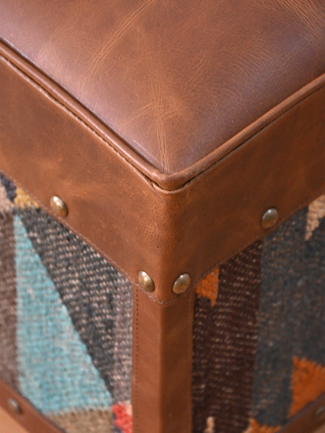 Close detail of the piped leather seat edge, leather-bound corner and studs on the Dundlod ottoman by Art Avenue