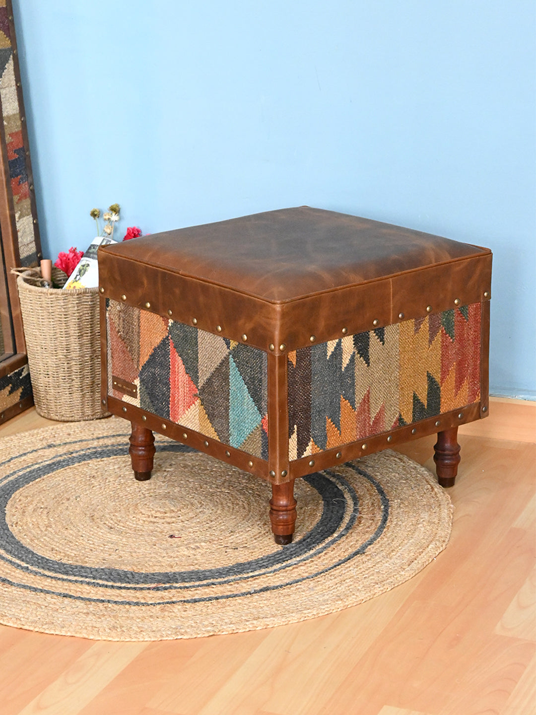 Dundlod kilim and leather ottoman by Art Avenue styled on a jute rug against a blue wall