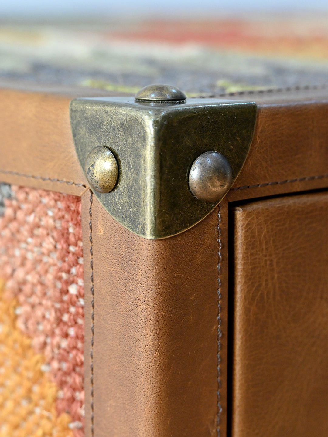 Close detail of an antique-brass corner cap on stitched leather, Kanota sideboard by Art Avenue