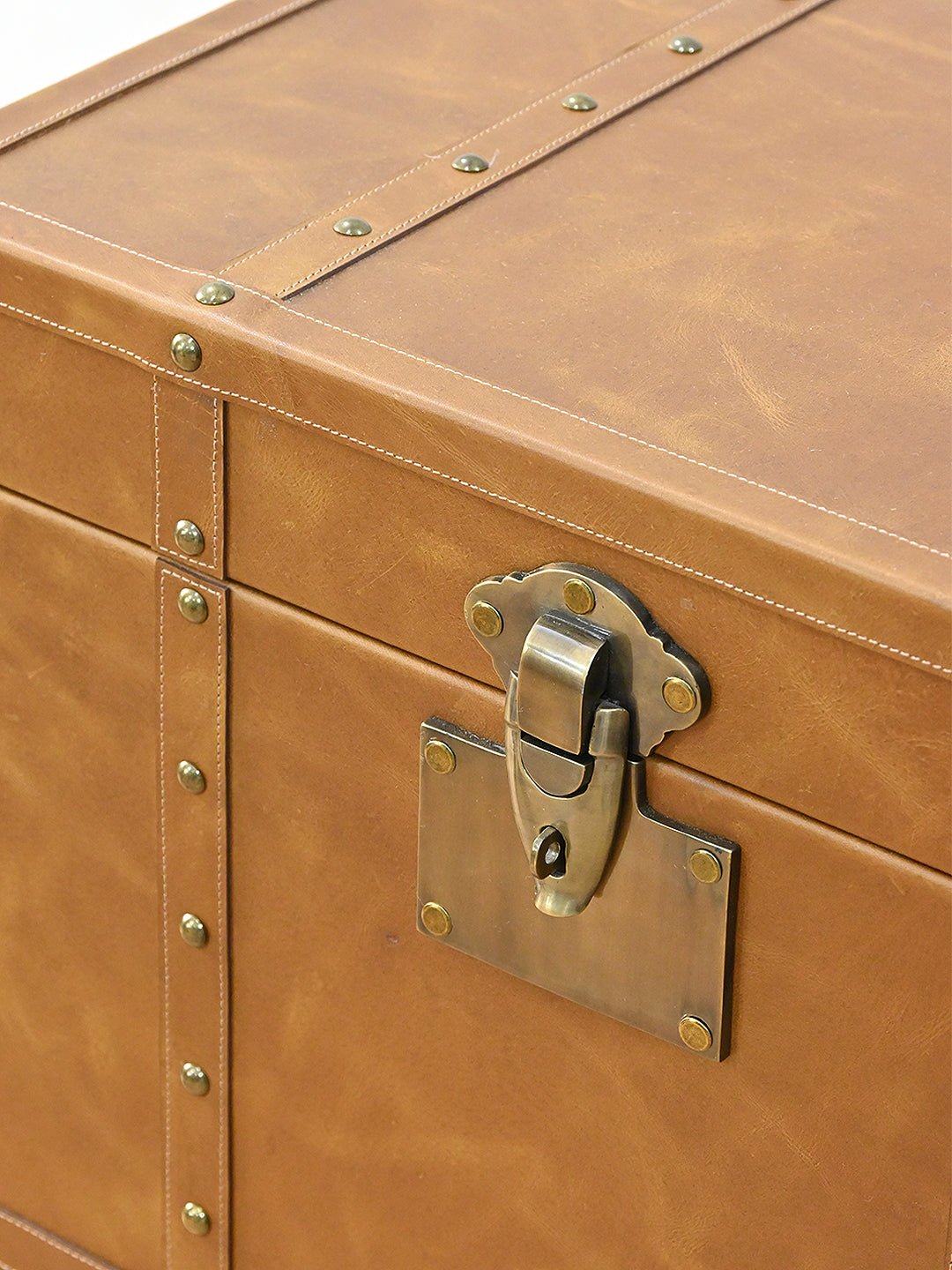 Close-up of the cast brass lock plate and swing catch on the leather lid of the Osian trunk, with domed studs along the stitched seams. Art Avenue, made to order.