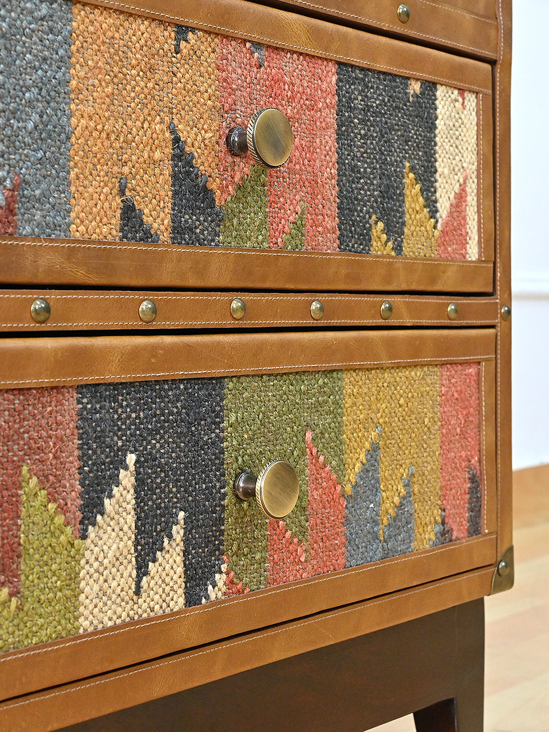 Detail of the Osian trunk's two kilim drawer fronts, each framed in stitched leather with a knurled brass knob, divided by a hand-studded leather band. Art Avenue, made to order.