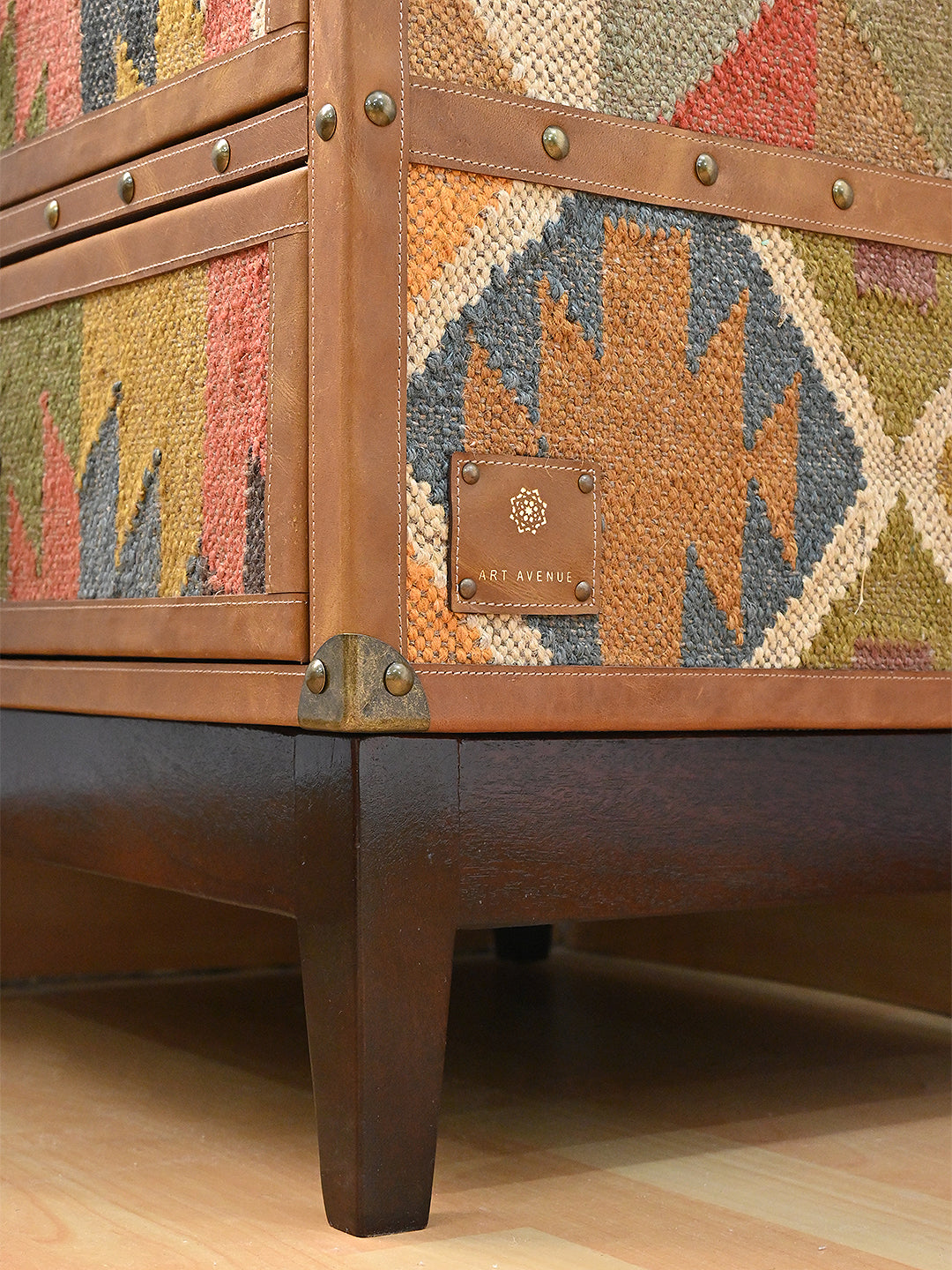 Art Avenue leather maker's tab stitched onto the vintage kilim flank of the Osian trunk, above the solid wood tapered leg. Made to order.