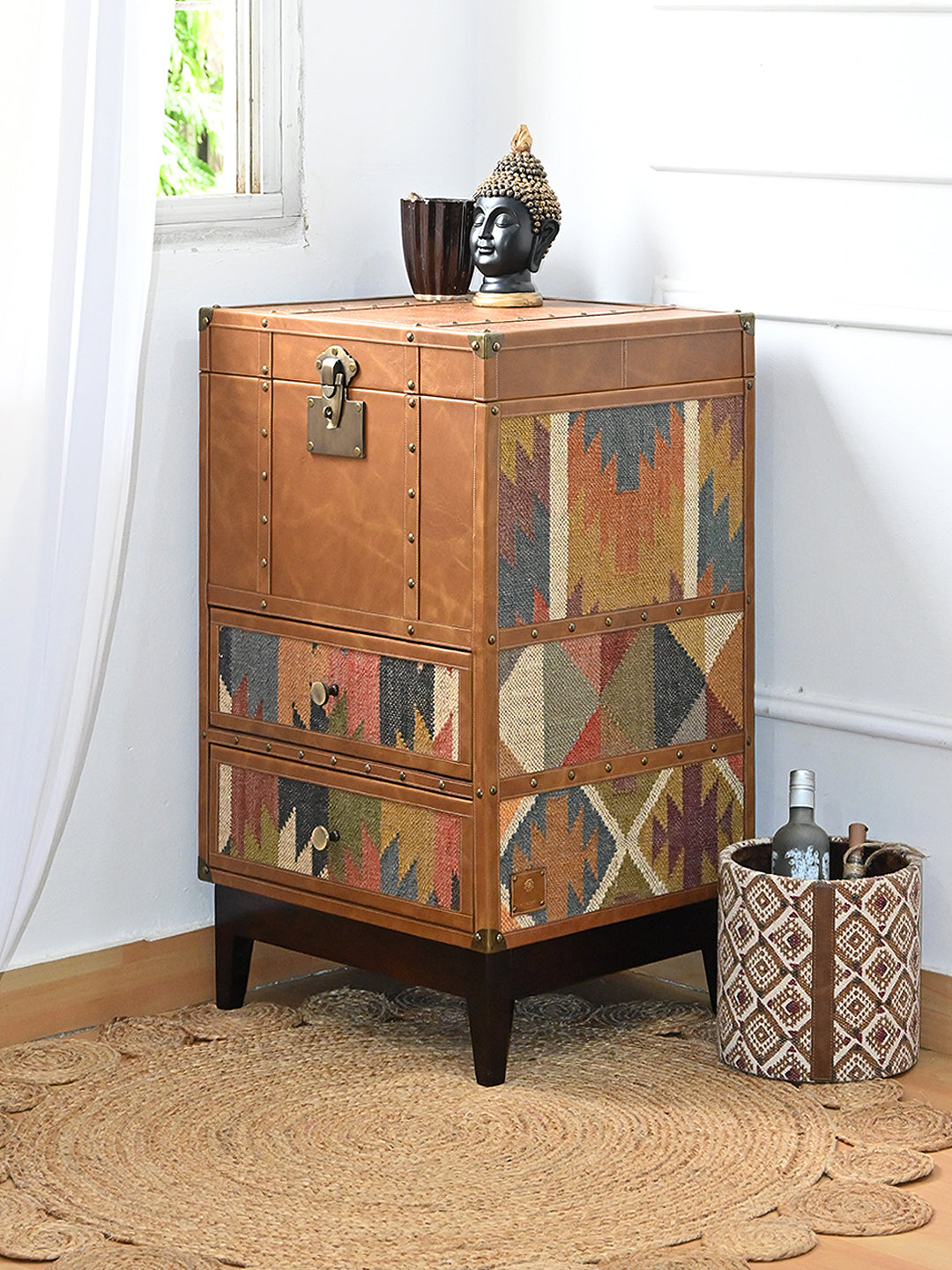 Osian kilim and leather drawer trunk styled in a corner with a Buddha head and planter resting on its leather top. Art Avenue, made to order.
