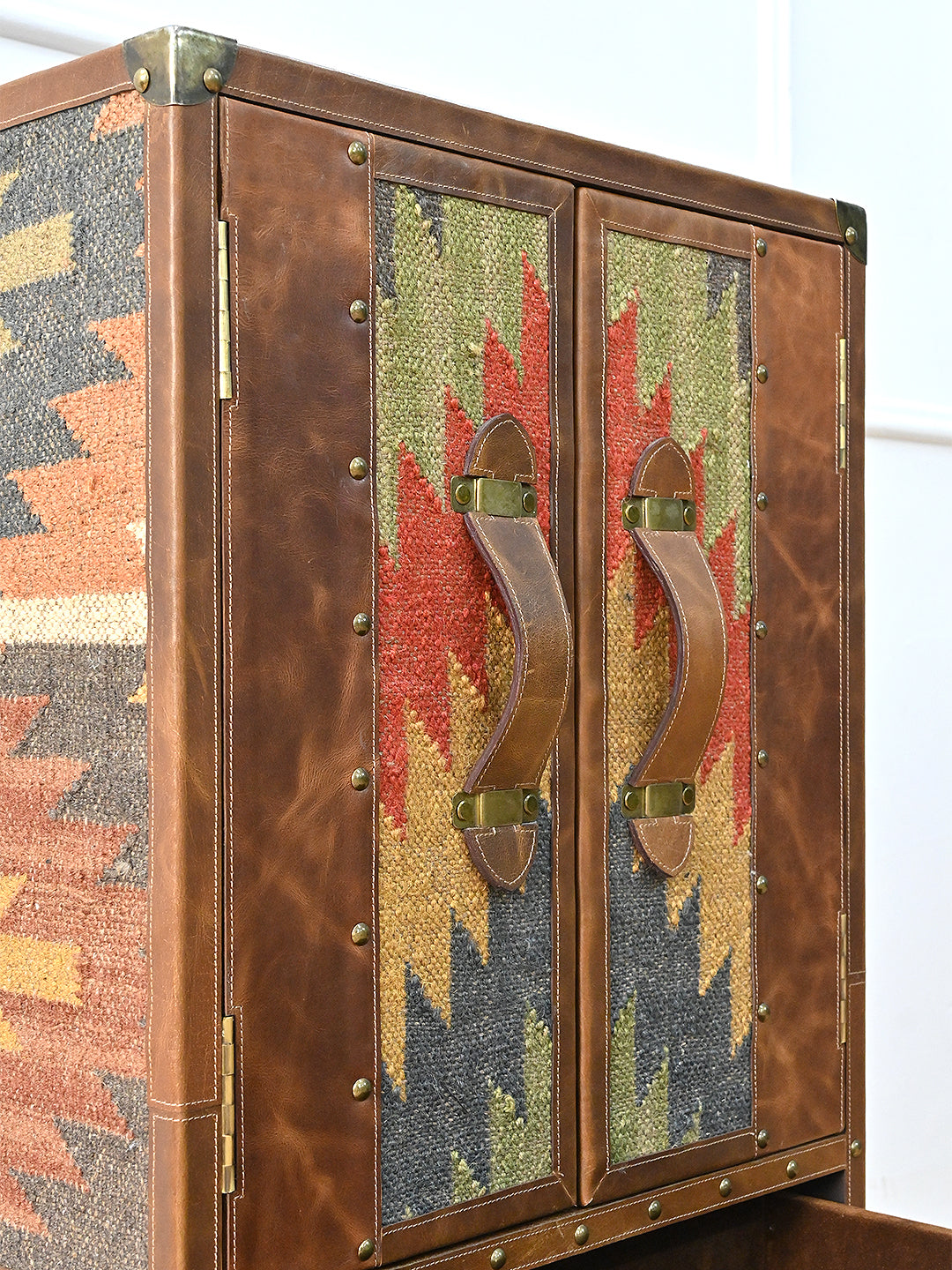 Close view of the Shalimar cabinet doors — kilim inset panels, leather strap pulls and a brass corner cap, Art Avenue