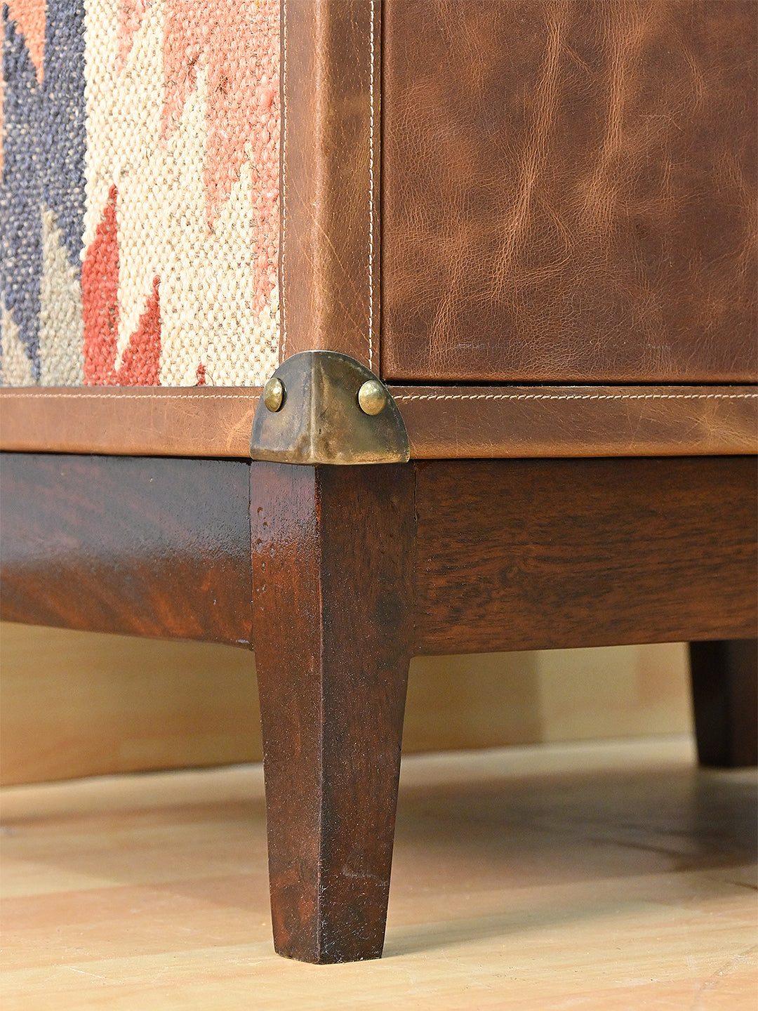 Detail of the half-round brass corner cap above the solid wood plinth and tapered leg — Art Avenue Shalimar cabinet