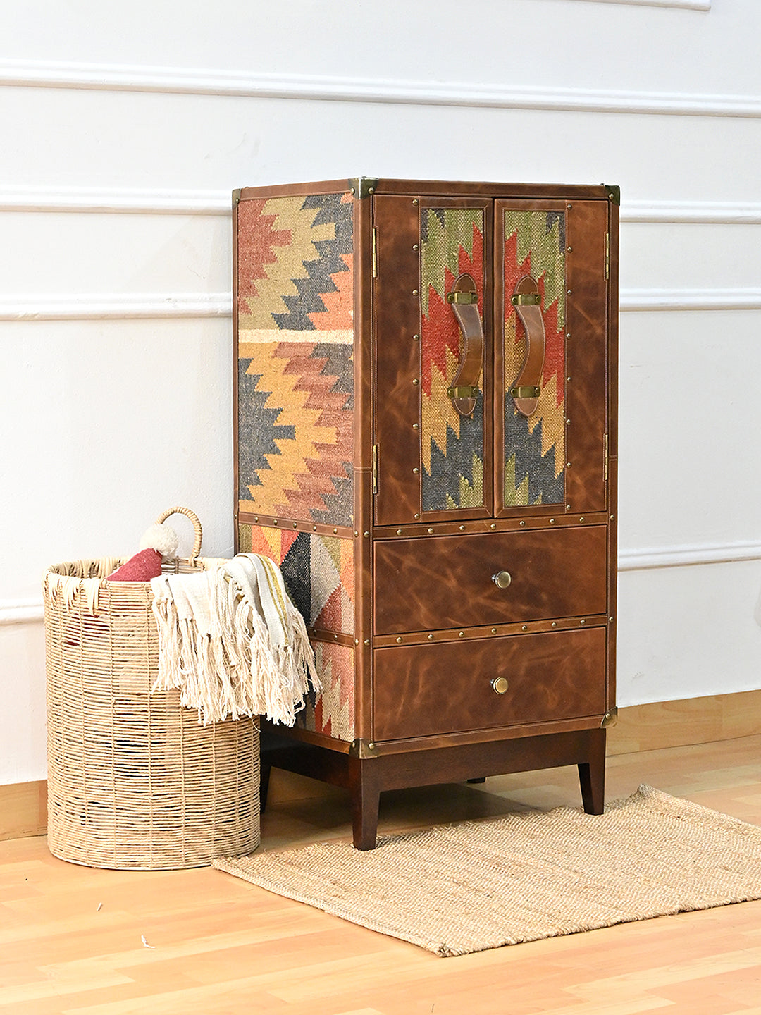 Shalimar cabinet at an angle, kilim flank and studded leather doors, with a woven basket alongside — Art Avenue